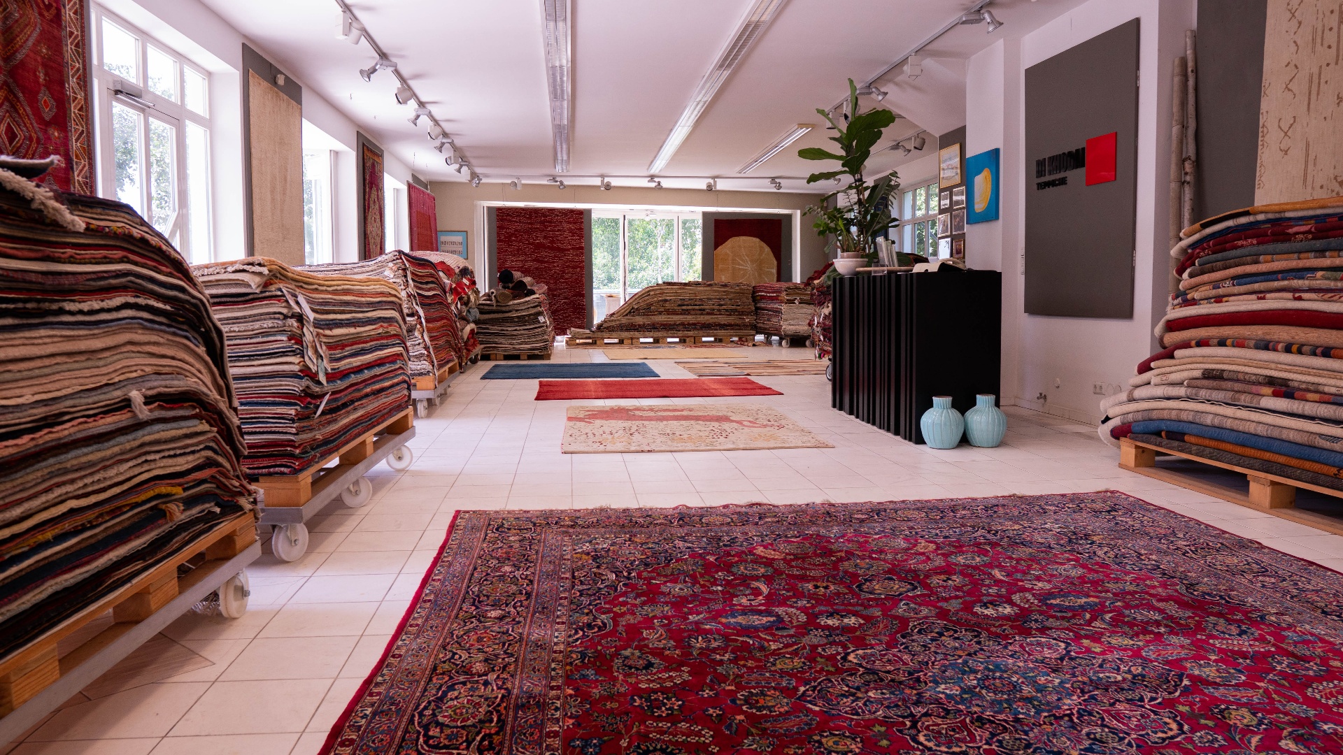 Showroom von Khodai in Graz mit gestapelten Orientteppichen und Tageslicht